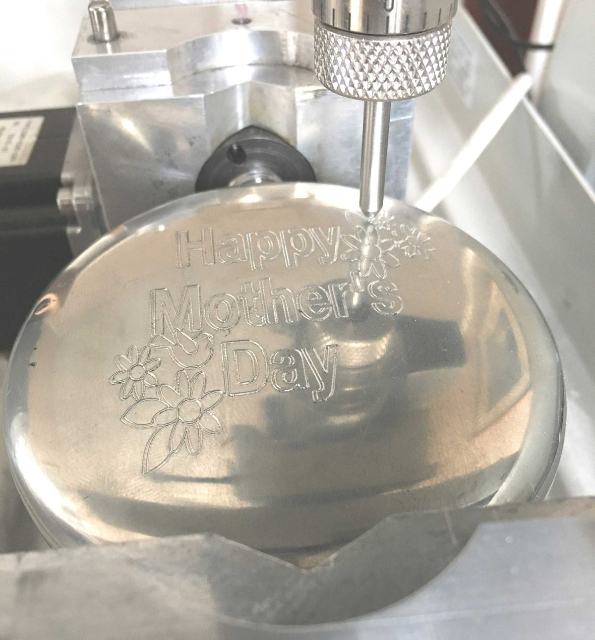 A pewter piece held in an engraving machine, part way through an inscription
